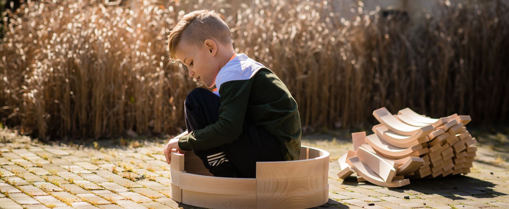 kind spielt mit ökologischen, naturbelassenen holzbausteinen von abel in herbstlichem garten
